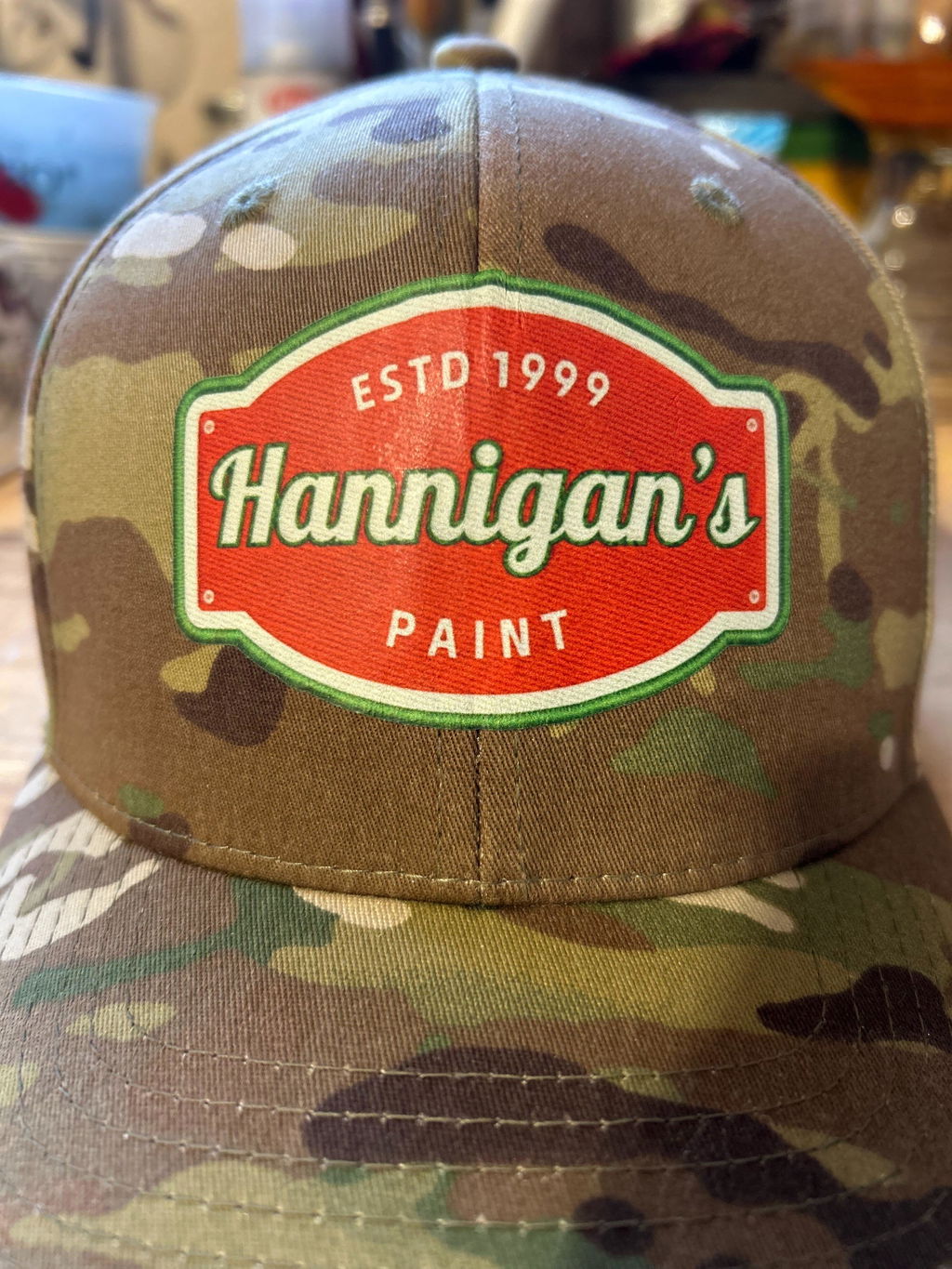 Camouflage cap with a red Hannigan's Paint emblem, from a customer review